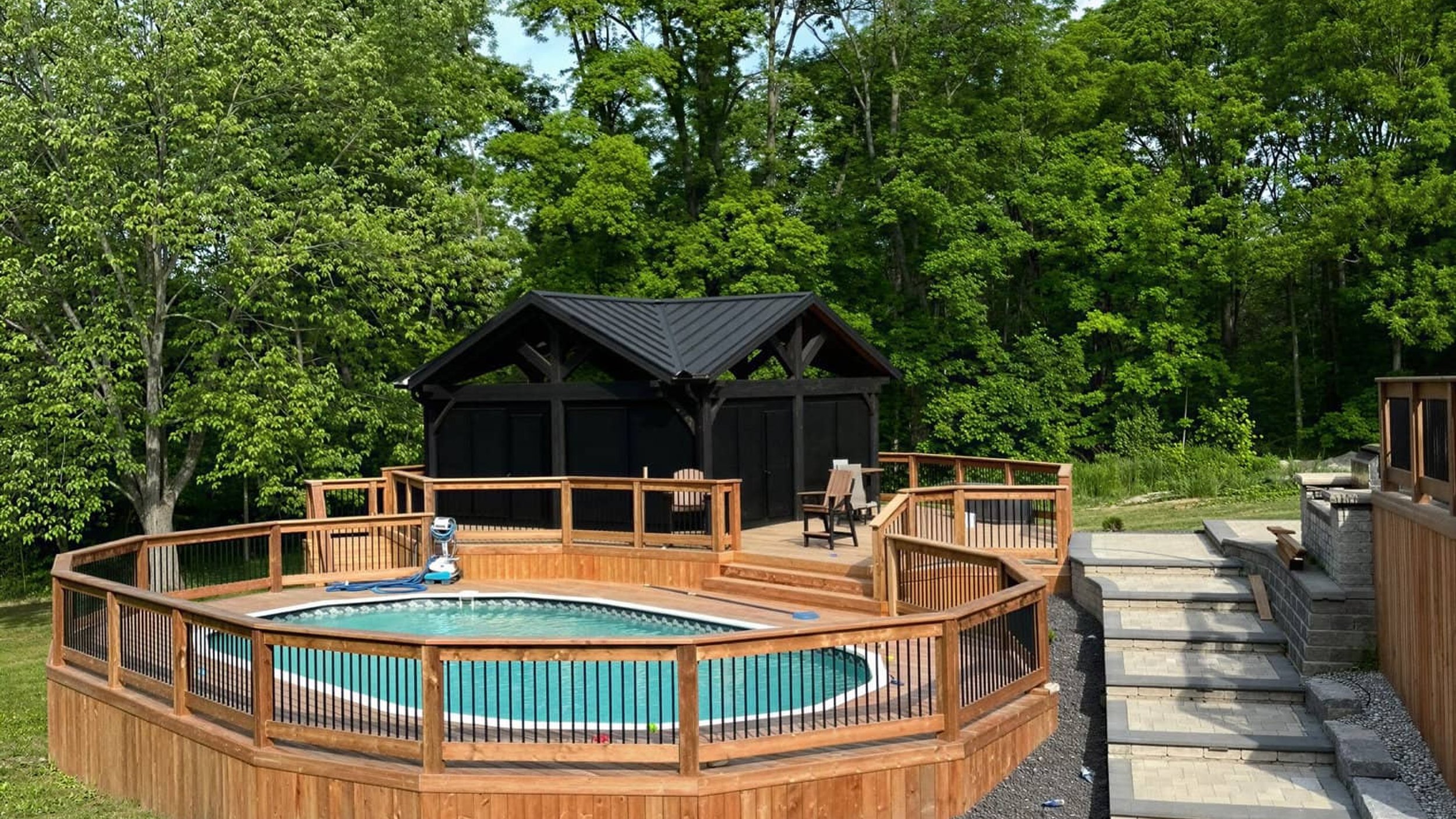 Cedar deck wrapping around above-ground pool with screened pavilion